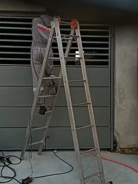 Serralheiro em cima de uma escada instalando um portão com veneziana